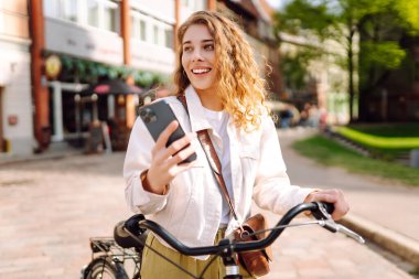 Bisiklet, kadın ve telefon şehirde heyecanlı ve mutlu bir şekilde yazları açık havada modaya uygun bir şekilde mesajlaşırken. Seyahat, hafta sonu, rahatlama ve yaşam tarzı konsepti. 