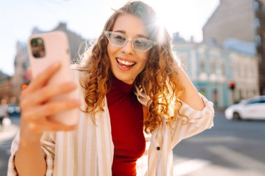 Güzel bir kadın kameraya bakar ve sokakta selfie çeker. Blogculuk, teknoloji, yaşam tarzı, seyahat, turizm, aktif yaşam.