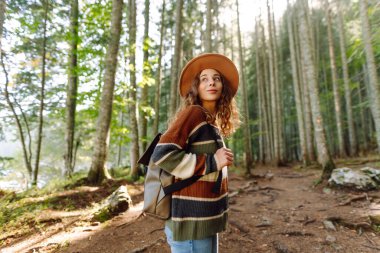 Sırt çantalı genç bir gezgin uzun kozalaklı ağaçlarla ormanda duruyor, doğanın tadını çıkarıyor. Hafta sonu, turizm. 