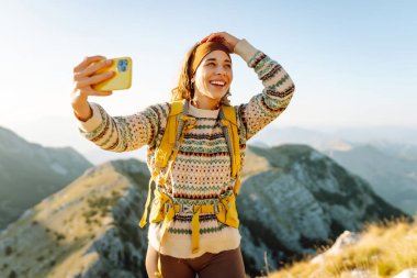 Genç bir kadın dağın tepesinde selfie portresi çekiyor. Yürüyüş, spor, seyahat ve teknoloji konsepti. 