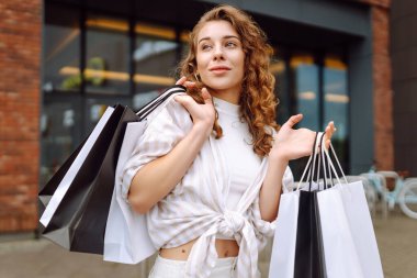 Alışveriş torbalı şık bir kadın şehrin sokaklarında yürüyor. Tüketim, moda, alışverişler, alışveriş, yaşam tarzı konsepti. 