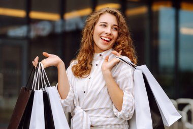 Alışveriş torbalı şık bir kadın şehrin sokaklarında yürüyor. Tüketim, moda, alışverişler, alışveriş, yaşam tarzı konsepti. 