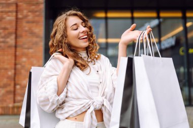 Alışveriş torbalı şık bir kadın şehrin sokaklarında yürüyor. Tüketim, moda, alışverişler, alışveriş, yaşam tarzı konsepti. 