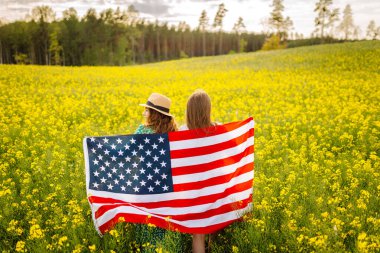 Amerikan bayrağı taşıyan iki genç kadın çiçek açan çayırda doğanın tadını çıkarıyorlar. 4 Temmuz. Bağımsızlık Günü.