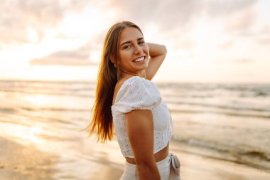 Genç bir kadın yaz günü gün batımında plaj okyanusunu seyretmekten zevk alıyor. Seyahat, hafta sonu, rahatlama ve yaşam tarzı konsepti. 