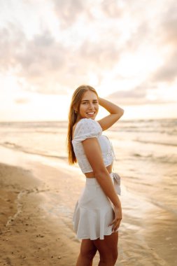 Genç bir kadın yaz günü gün batımında plaj okyanusunu seyretmekten zevk alıyor. Seyahat, hafta sonu, rahatlama ve yaşam tarzı konsepti. 