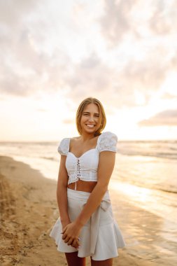 Genç bir kadın yaz günü gün batımında plaj okyanusunu seyretmekten zevk alıyor. Seyahat, hafta sonu, rahatlama ve yaşam tarzı konsepti. 