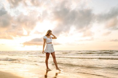 Genç bir kadın yaz günü gün batımında plaj okyanusunu seyretmekten zevk alıyor. Seyahat, hafta sonu, rahatlama ve yaşam tarzı konsepti. 