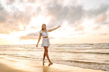 Genç bir kadın yaz günü gün batımında plaj okyanusunu seyretmekten zevk alıyor. Seyahat, hafta sonu, rahatlama ve yaşam tarzı konsepti. 