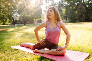 Spor giyim bölümünde genç bir kadın parktaki spor minderinde vücut esnetiyor, yoga yapıyor. Sağlıklı yaşam tarzı, spor. Fitness. Sabah parkında yoga yapan kadın..