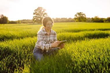 Akıllı çiftlik. Yeşil tarlada tabletli bir kadın çiftçi. Çiftçilik ve sulama kavramı.