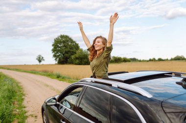 Elleri havada arabadan sarkan genç bir kadın doğada taze yaz rüzgarının tadını çıkarıyor. Yaz gezisi. Yaşam tarzı, seyahat, turizm, doğa, aktif yaşam