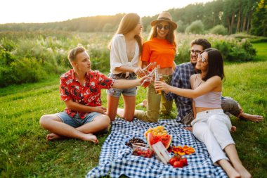 Parkta piknik yapan mutlu genç arkadaşlar. Bira içerken eğlenen bir grup genç, güneşli günün tadını çıkarın. Tatil, hafta sonu, arkadaşlık ya da tatil konsepti. 