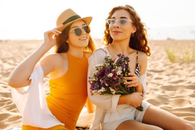 İki güzel genç kadın sahilde eğleniyor. Plajda yürüyen ve yaz günü gülen kadın arkadaşlar. Seyahat, hafta sonu, rahatlama ve yaşam tarzı konsepti.