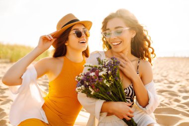 İki güzel genç kadın sahilde eğleniyor. Plajda yürüyen ve yaz günü gülen kadın arkadaşlar. Seyahat, hafta sonu, rahatlama ve yaşam tarzı konsepti.