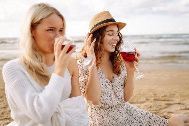 İki kadın arkadaş, deniz kenarında oturmuş şarapla piknik yapıyorlar. Tatil, rahatla, bekarlığa veda partisi