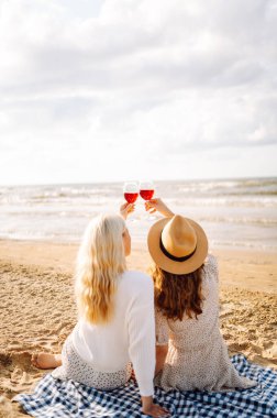 İki kadın arkadaş, deniz kenarında oturmuş şarapla piknik yapıyorlar. Tatil, rahatla, bekarlığa veda partisi