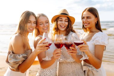 Şarap kadehleriyle gülümseyen genç bayanlar sahilde durup, bekarlığa veda partisini kutluyor, gün batımında pikniğin tadını çıkarıyorlar. Tatil, rahatla.