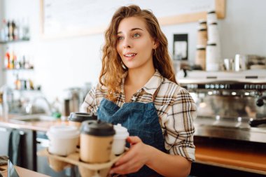 Kafe restoranındaki tezgahın arkasında duran tüketiciye sıcak kahve bardağı servisi yapan genç bayan barista. Küçük işletme, yiyecek ve içecek, hizmet zihin konsepti.