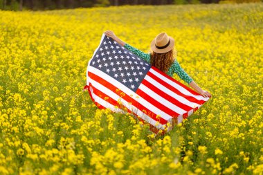 Tarlada rüzgarda Amerikan bayrağı tutan güzel bir genç kadın. Vatansever bayram. ABD 4 Temmuz 'u kutladı.