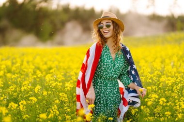Tarlada rüzgarda Amerikan bayrağı tutan güzel bir genç kadın. Vatansever bayram. ABD 4 Temmuz 'u kutladı.