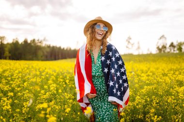 Tarlada rüzgarda Amerikan bayrağı tutan güzel bir genç kadın. Vatansever bayram. ABD 4 Temmuz 'u kutladı.