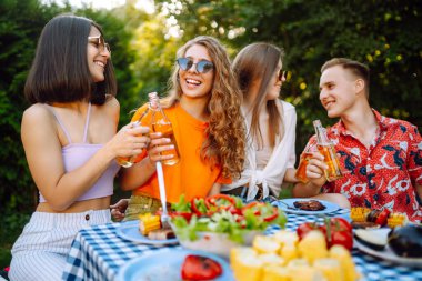 Bir grup mutlu genç arkadaş dışarıda piknik yapıyor. İnsanlar barda ızgara yaparken eğleniyor ve kutluyorlar. Tatil, piknik, hafta sonu, doğa