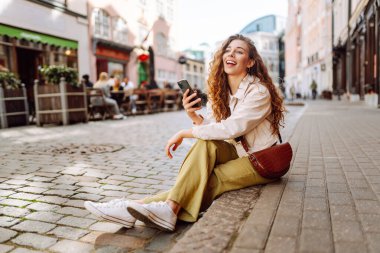 Şehir caddesinde telefonla yürüyen mutlu bir kadın. Yaşam tarzı, seyahat, turizm, teknoloji, blog yazma, iletişim kavramı.
