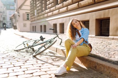 Sokak şehrinde bisikletin yanında oturan güzel, gülümseyen kadın. Macera Konsepti