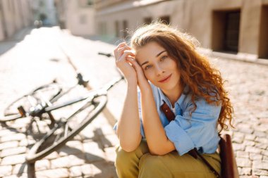 Sokak şehrinde bisikletin yanında oturan güzel, gülümseyen kadın. Macera Konsepti