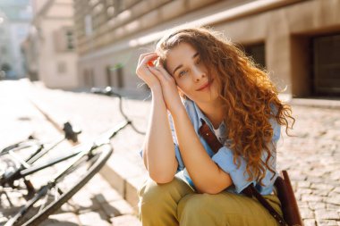 Sokak şehrinde bisikletin yanında oturan güzel, gülümseyen kadın. Macera Konsepti