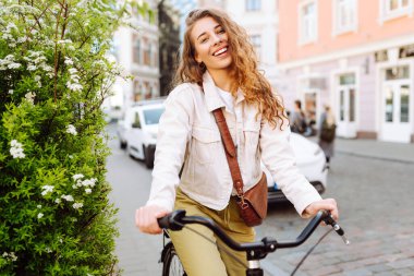 Güneşli bir günde, şehrin caddesinde bisikletle poz veren güzel bir genç kadın. Aktif yaşam tarzı. Eko taşımacılığı.