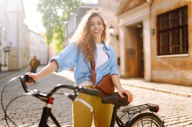 Güneşli bir günde, şehrin caddesinde bisikletle poz veren güzel bir genç kadın. Aktif yaşam tarzı. Eko taşımacılığı.