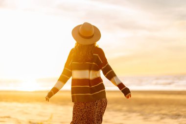 Güzel kıvırcık kadın kumsalda, soğuk güneşli havada, derin nefes alan taze okyanus esintisi. Bahar geldi. Seyahat, hafta sonu, rahatlama ve yaşam tarzı konsepti.