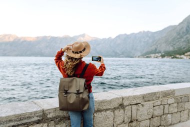 Seyahat blogcusu akıllı telefon kamerasında fotoğraf çekiyor. Dağları, okyanusu ve günbatımını gösteren muhteşem bir manzara. Tatil sırasında akıllı telefondan. Tatillerde turist