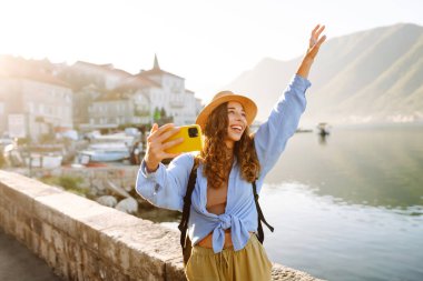 Güzel genç kız güneşli havanın tadını çıkarıyor. Sosyal ağdaki haberi için akıllı telefondan selfie çeken bir kadın. Yaşam tarzı olarak seyahat etmek.