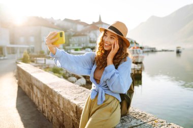 Güzel genç kız güneşli havanın tadını çıkarıyor. Sosyal ağdaki haberi için akıllı telefondan selfie çeken bir kadın. Yaşam tarzı olarak seyahat etmek.