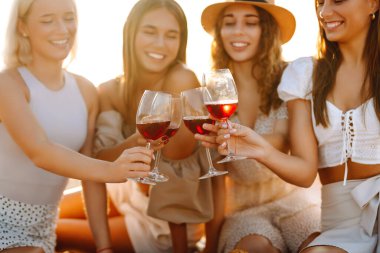 Kumsalda kızlar partisi. Genç bayanlar, ellerinde şarap kadehleriyle sahilde poz veriyorlar. Tatil, rahatla..