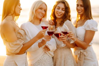 Kumsalda kızlar partisi. Genç bayanlar, ellerinde şarap kadehleriyle sahilde poz veriyorlar. Tatil, rahatla..