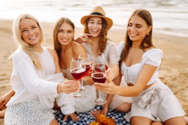 Kumsalda kızlar partisi. Genç bayanlar, ellerinde şarap kadehleriyle sahilde poz veriyorlar. Tatil, rahatla..