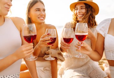 Kumsalda kızlar partisi. Genç bayanlar, ellerinde şarap kadehleriyle sahilde poz veriyorlar. Tatil, rahatla..