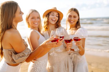 Kumsalda kızlar partisi. Genç bayanlar, ellerinde şarap kadehleriyle sahilde poz veriyorlar. Tatil, rahatla..