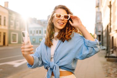 Günbatımında sokakta poz veren tasasız bir model. Pov özçekim videoları çeken esmer bir kadın. Teknoloji, blog yazma, iletişim kavramı.