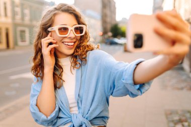 Günbatımında sokakta poz veren tasasız bir model. Pov özçekim videoları çeken esmer bir kadın. Teknoloji, blog yazma, iletişim kavramı.