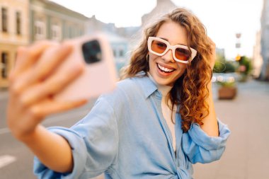 Günbatımında sokakta poz veren tasasız bir model. Pov özçekim videoları çeken esmer bir kadın. Teknoloji, blog yazma, iletişim kavramı.