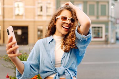 Günbatımında sokakta poz veren tasasız bir model. Pov özçekim videoları çeken esmer bir kadın. Teknoloji, blog yazma, iletişim kavramı.