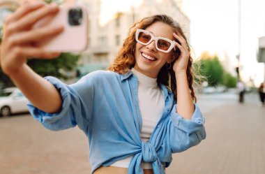 Günbatımında sokakta poz veren tasasız bir model. Pov özçekim videoları çeken esmer bir kadın. Teknoloji, blog yazma, iletişim kavramı.