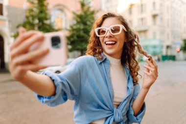 Günbatımında sokakta poz veren tasasız bir model. Pov özçekim videoları çeken esmer bir kadın. Teknoloji, blog yazma, iletişim kavramı.