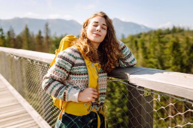  Ağaçların arasında sırt çantasıyla tahta köprüde bir kadın. Özgürlük kavramı, seyahat, yaşam tarzı. Keyifli dağların manzarası, yaz tatili.