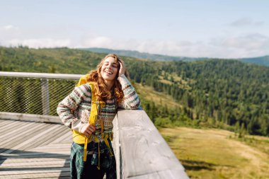  Ağaçların arasında sırt çantasıyla tahta köprüde bir kadın. Özgürlük kavramı, seyahat, yaşam tarzı. Keyifli dağların manzarası, yaz tatili.